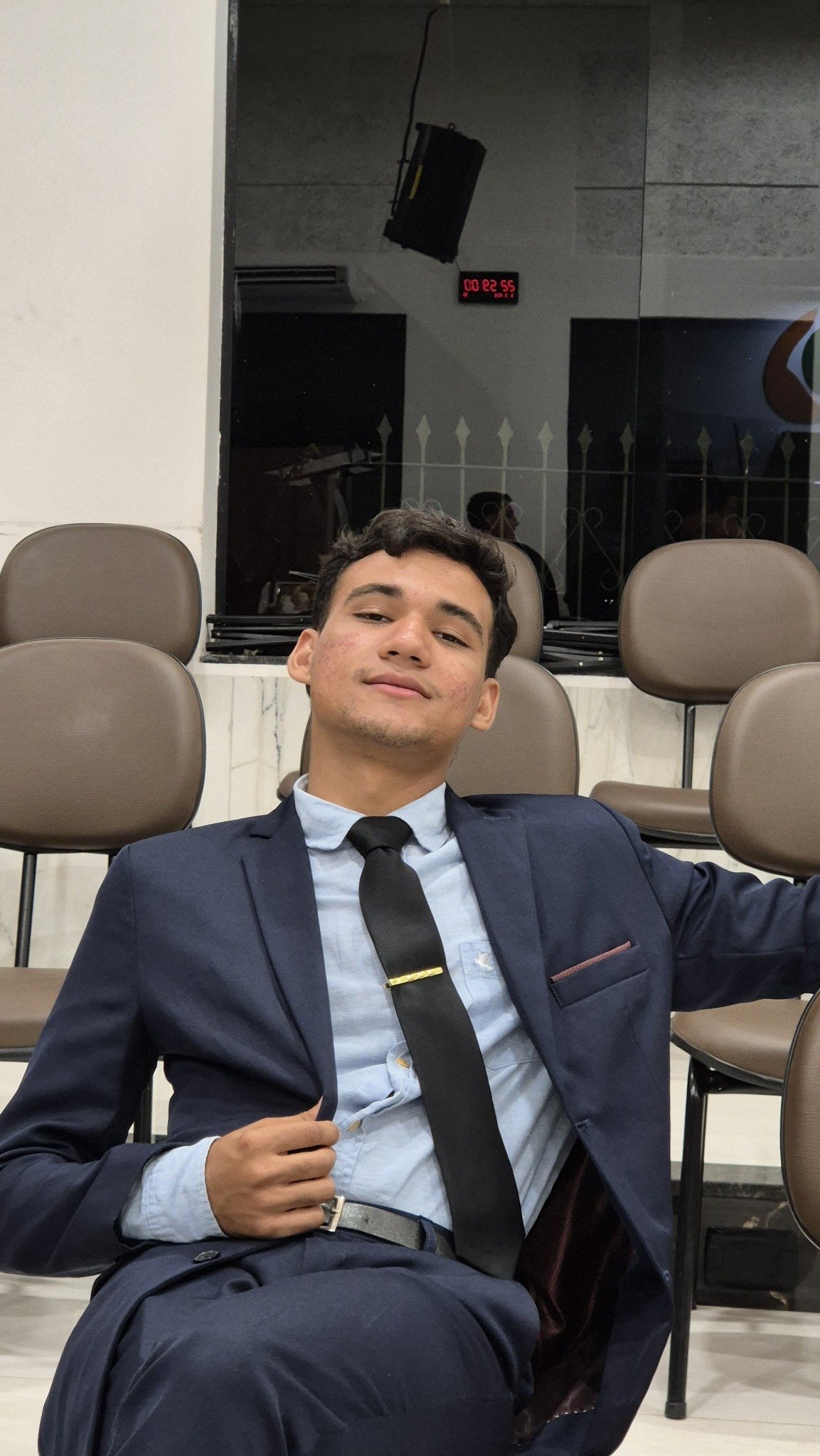 Rhuan usando terno, em uma sala de auditório